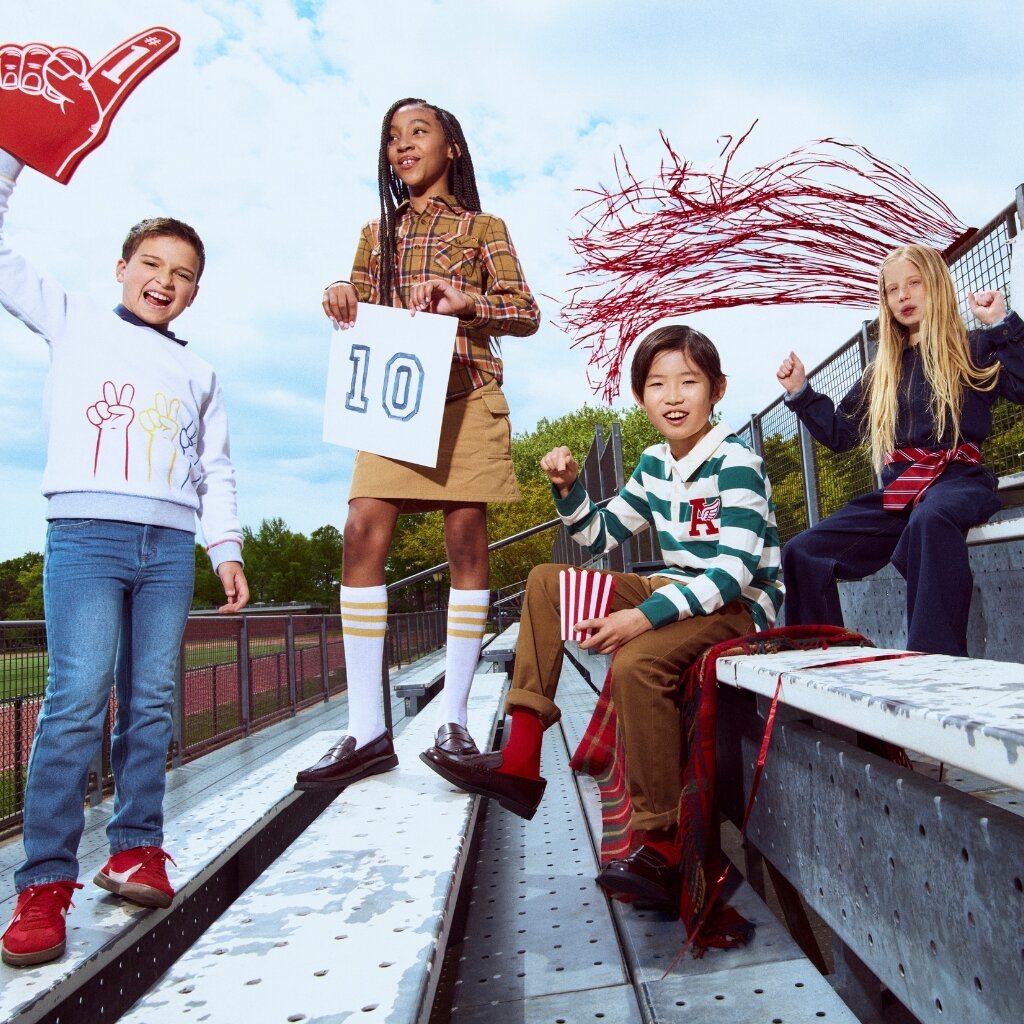 Four children in colorful outfits on a bridge with a clear blue sky.