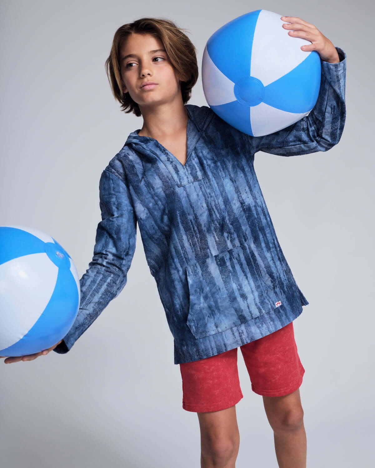 High-quality kids clothing featuring a boy in a blue striped hoodie and red shorts, holding beach balls.